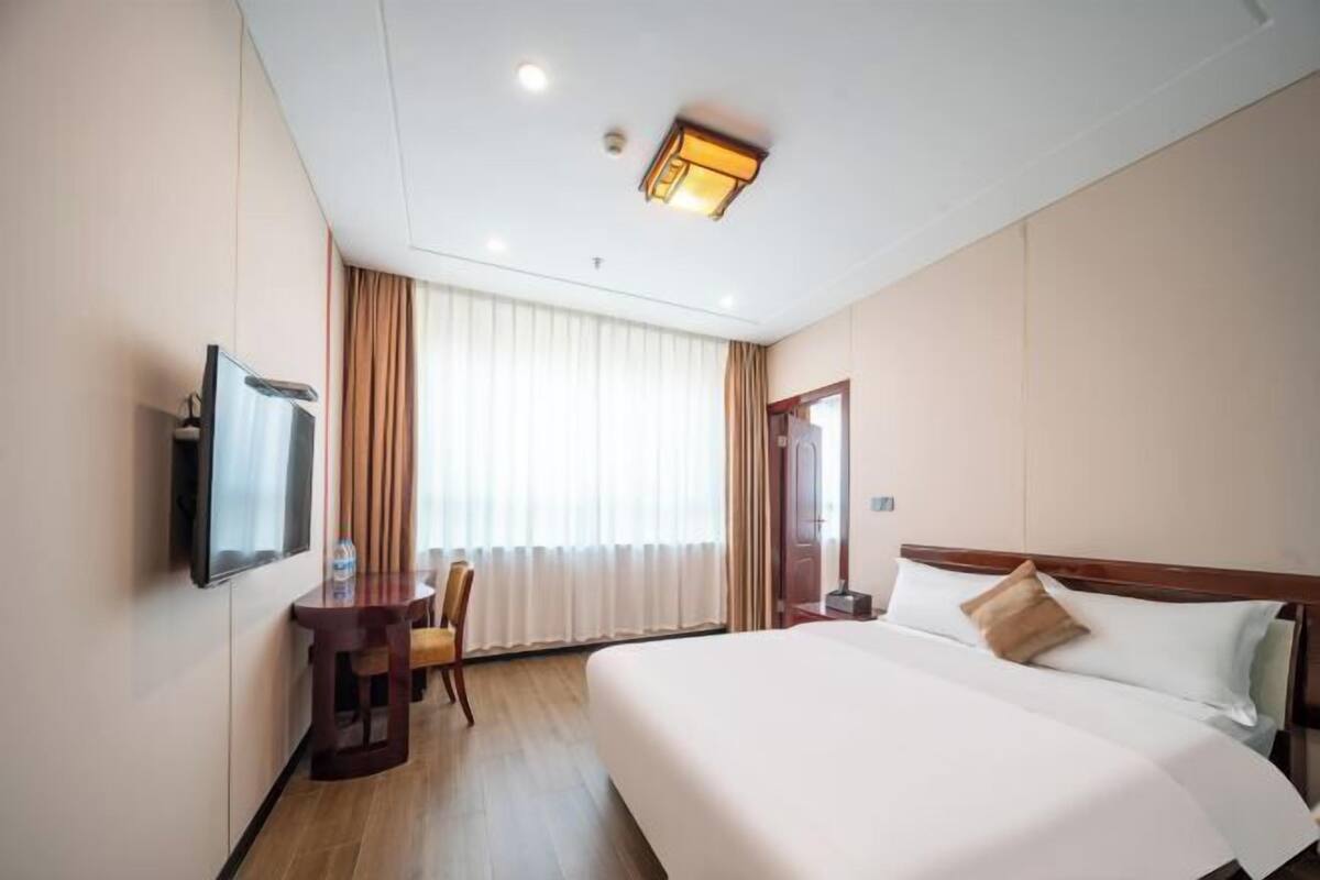 Ein Hotelzimmer mit einem großen Bett, einem Schreibtisch, einem Sessel, einem Fernseher und einem Fenster mit Vorhängen.