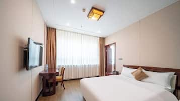 A hotel room with a large bed, a desk with a chair, a television, and a window with curtains.