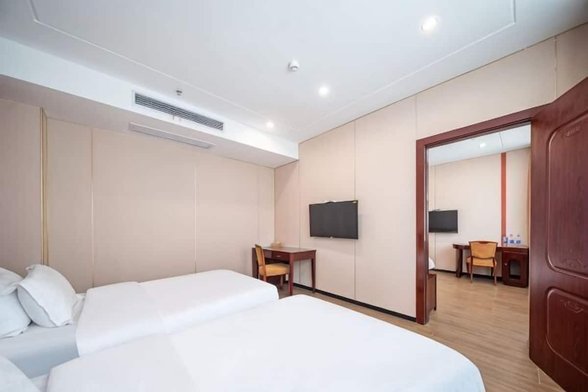 Ein Hotelzimmer mit zwei Betten, einem Schreibtisch, einem Stuhl, einem Fernseher und einem Spiegel.