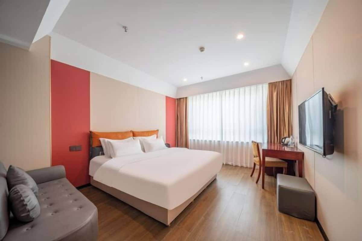 Ein Hotelzimmer mit Bett, Schreibtisch, Stuhl, Fernseher und einem Fenster mit Vorhängen.