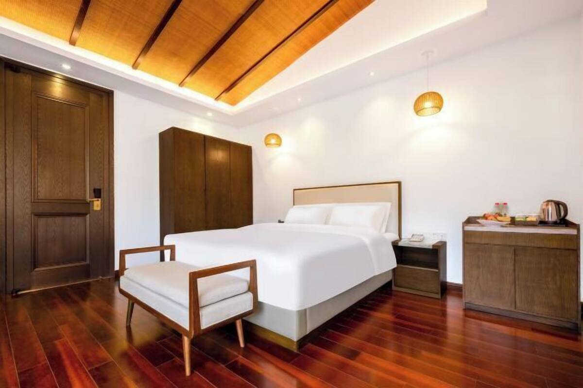 Habitación de hotel con cama, mesita de noche, silla, armario y kitchenette.