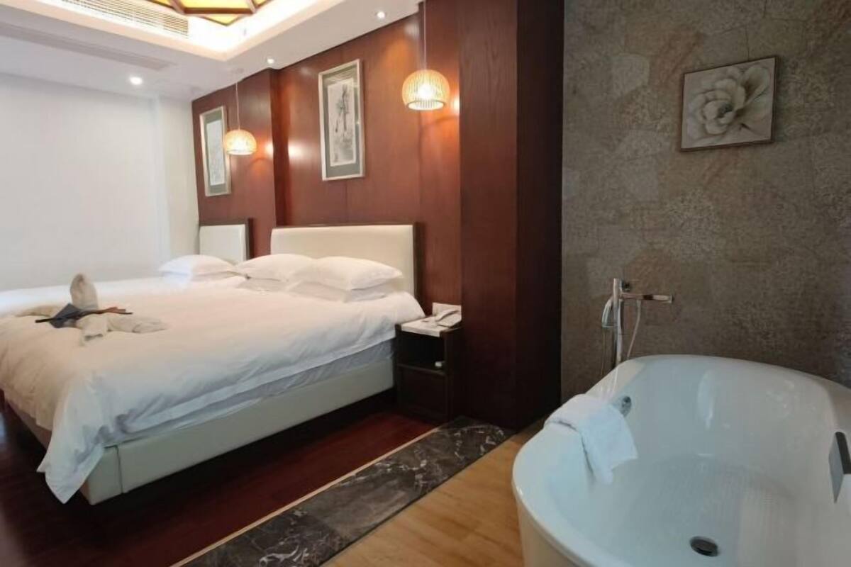 Habitación de hotel con una cama grande, baño independiente con bañera y suelo de madera.