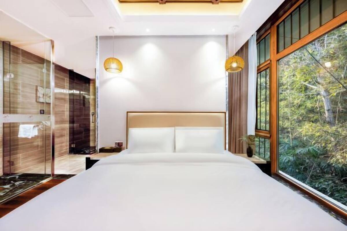 Un dormitorio moderno con una cama grande, dos lámparas fijadas a la pared y vistas a la vegetación a través de un ventanal.