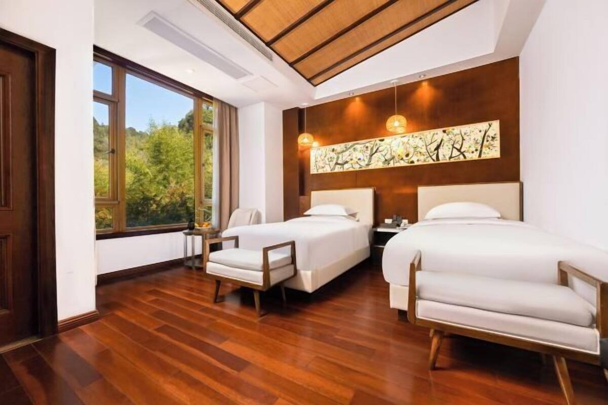Una habitación de hotel moderna con dos camas, un ventanal grande y techo de madera.