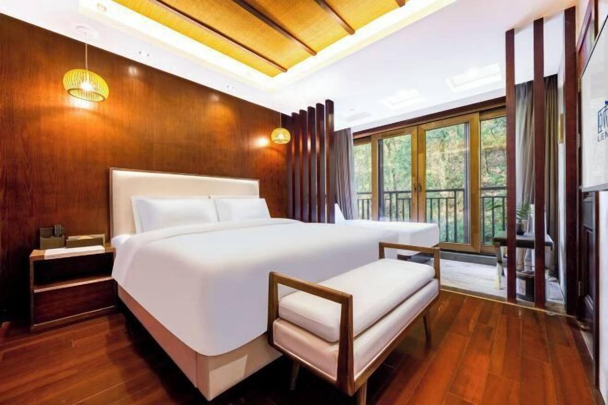Habitación de hotel moderna con una cama grande, suelo de madera, una mesita de noche y vistas al exterior.