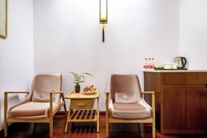 Une pièce comprenant deux chaises, une petite table avec une plante, un luminaire fixé au mur et un coin cuisine avec une bouilloire et des bouteilles.