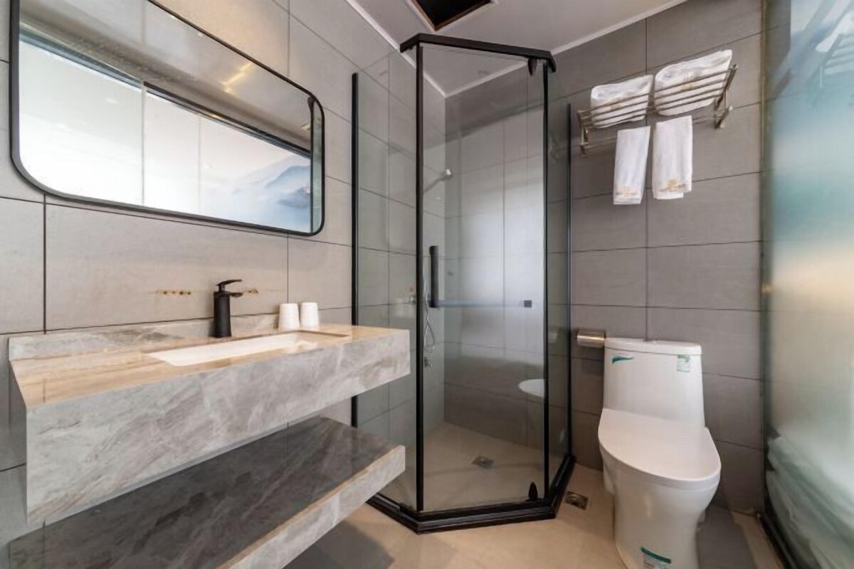 A modern bathroom with a glass-enclosed shower, a marble vanity, and a toilet.