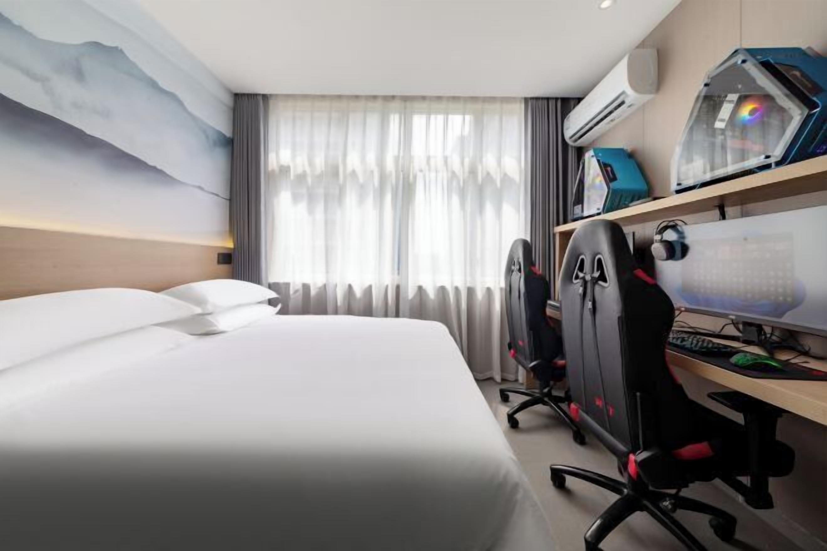 Habitación de hotel con cama, escritorio, computadora, silla y aire acondicionado.