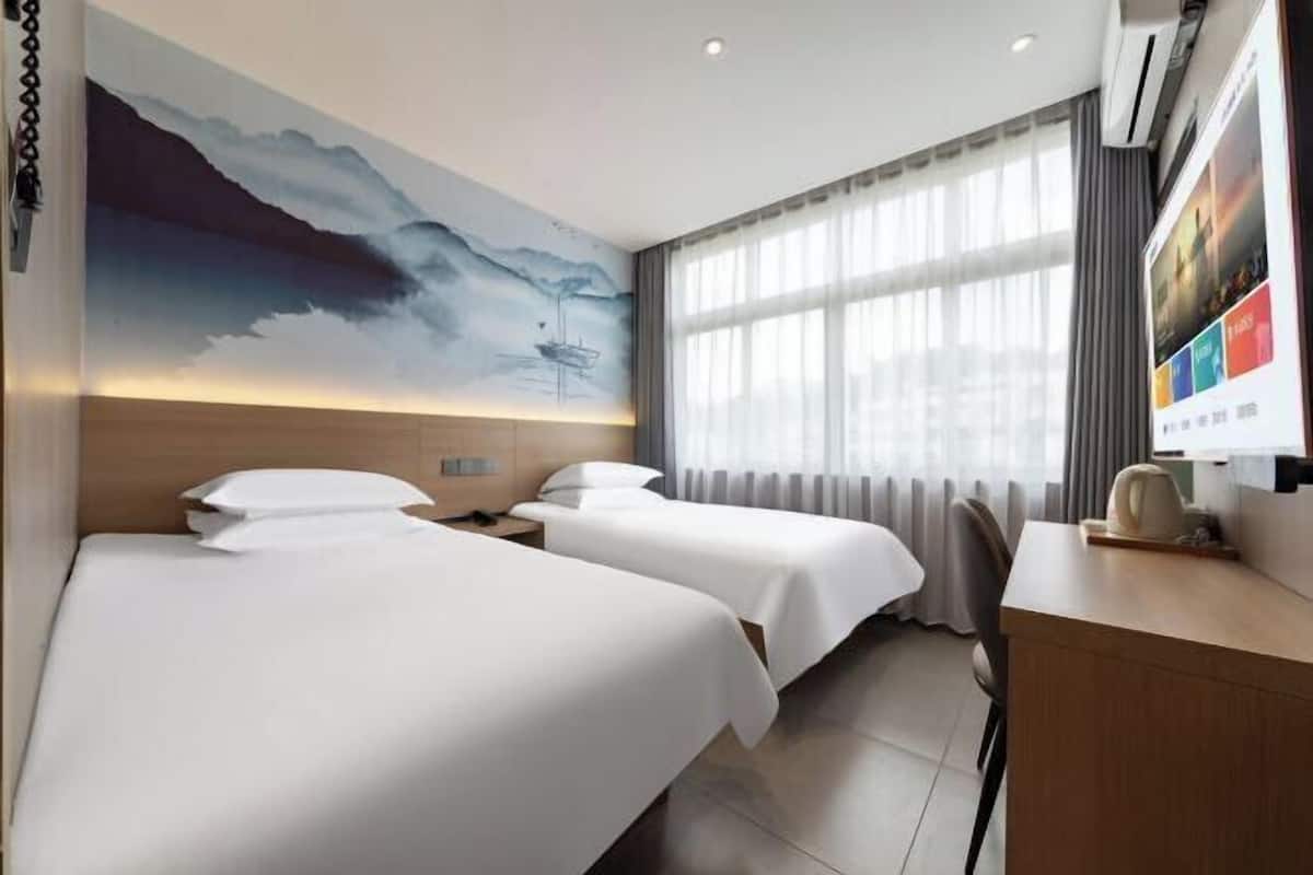 Habitación de hotel con dos camas, un escritorio, una silla, un ventanal con cortinas y un mural en la pared.