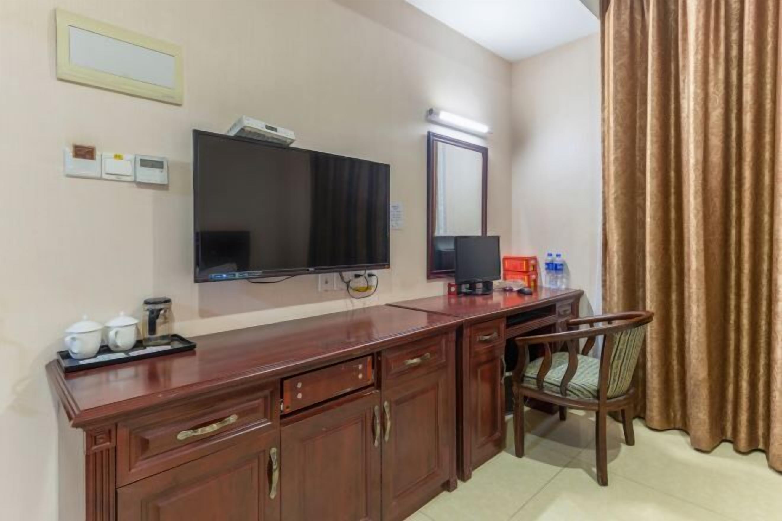 Habitación de hotel con un escritorio de madera, un televisor, un espejo y una silla.