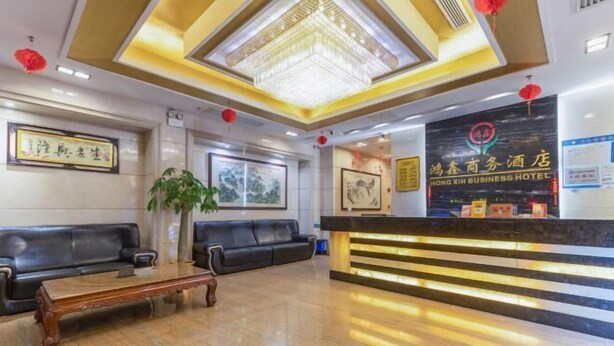 A hotel reception area with a reception desk, black leather sofas, a wooden coffee table, and a large chandelier. - Hong Xin Business Hotel (Guangzhou)