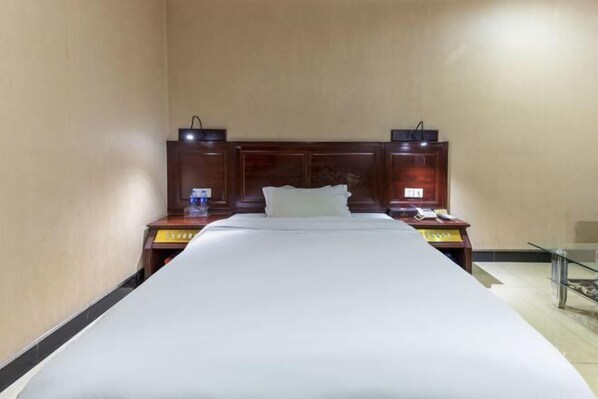 A hotel room with a single bed, a nightstand with a lamp, a telephone, and a small table with a glass top. - Hong Xin Business Hotel (Guangzhou)