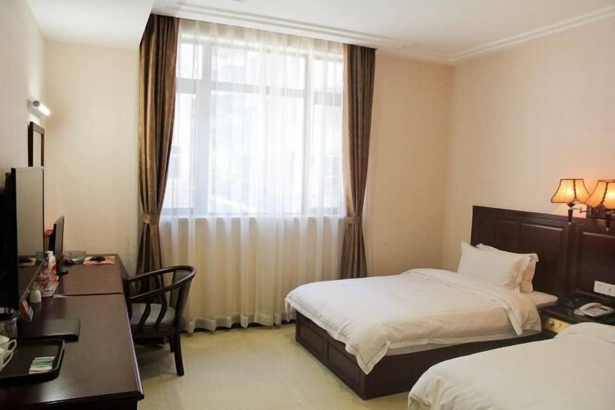 A hotel room with a bed, a desk with a chair, a lamp, and a window with curtains.