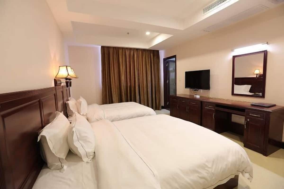 A hotel room with two beds, a desk, a television, and a mirror.