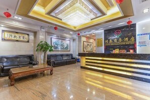 A hotel lobby with a reception desk, black leather sofas, a wooden coffee table, and a chandelier.