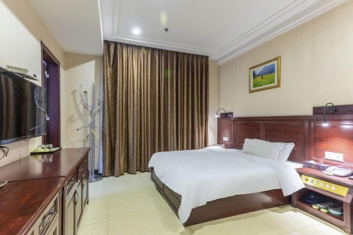 A hotel room with a bed, a TV, a desk, a wardrobe, a curtain, and a painting on the wall.
