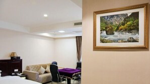 A hotel room with a bed, a sofa, a dining table with chairs, a desk, and a framed painting on the wall. - Hong Xin Business Hotel (Guangzhou)