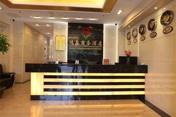 A hotel reception desk with a black marble counter, a logo above it, and a wall with framed awards. - Hong Xin Business Hotel (Guangzhou)
