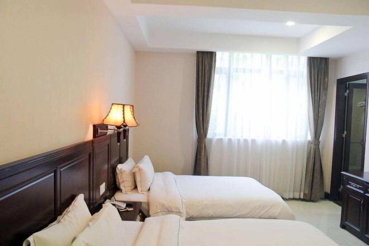 A hotel room with two beds, a nightstand, a lamp, a wardrobe, and a window with curtains.