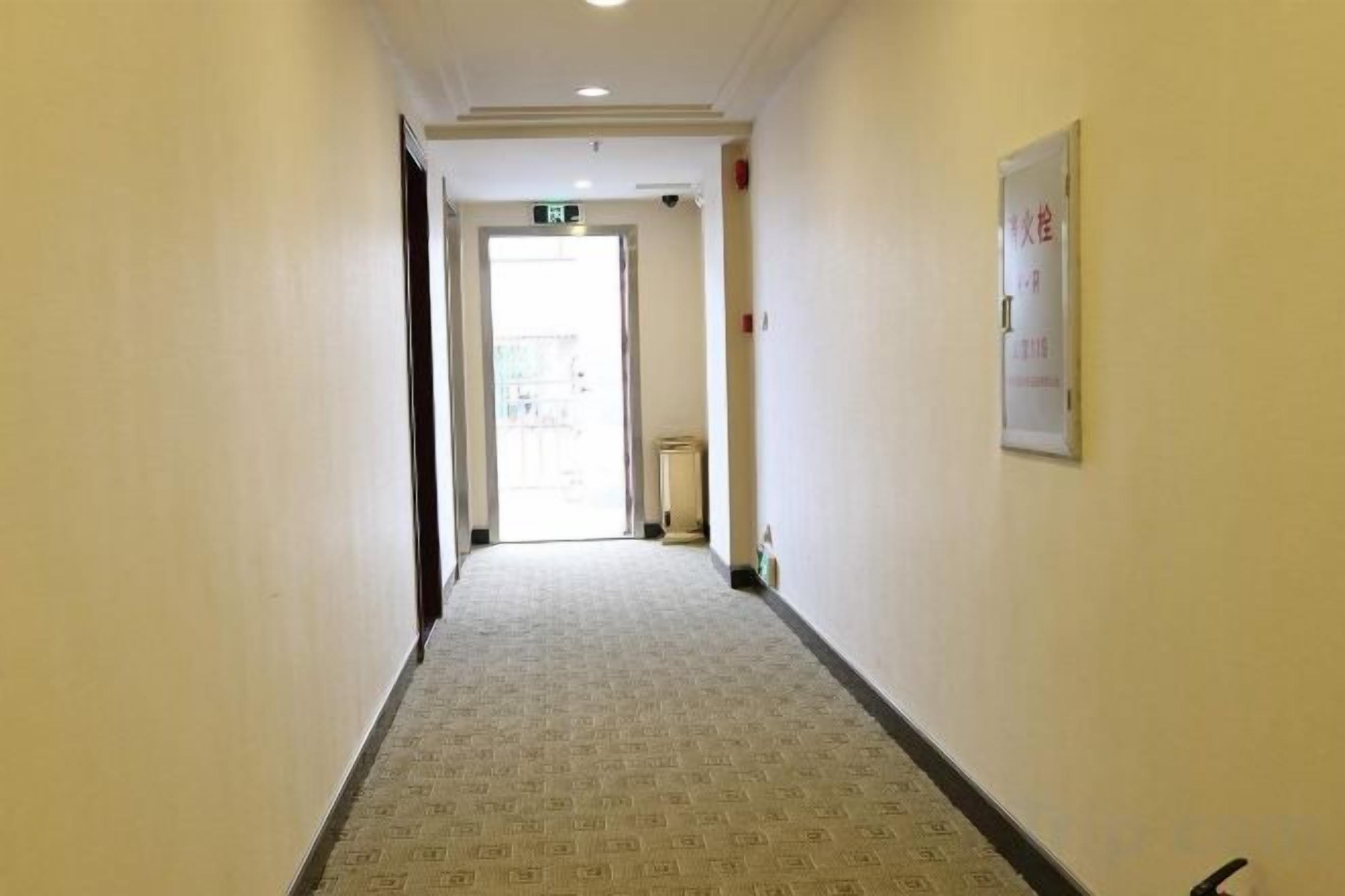Ein schmaler Flur mit einem gemusterten Teppich, einer Tür am Ende und einem Schild an der Wand.