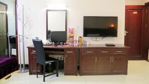 A hotel room with a wooden desk, a chair, a flat-screen TV mounted on the wall, a cabinet, and a door. - Hong Xin Business Hotel (Guangzhou)