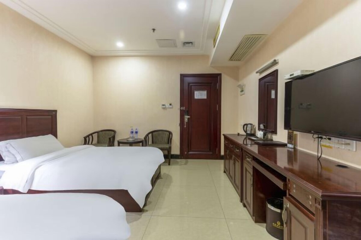 A hotel room with two beds, a TV, a desk with a chair, and a small table with a kettle.