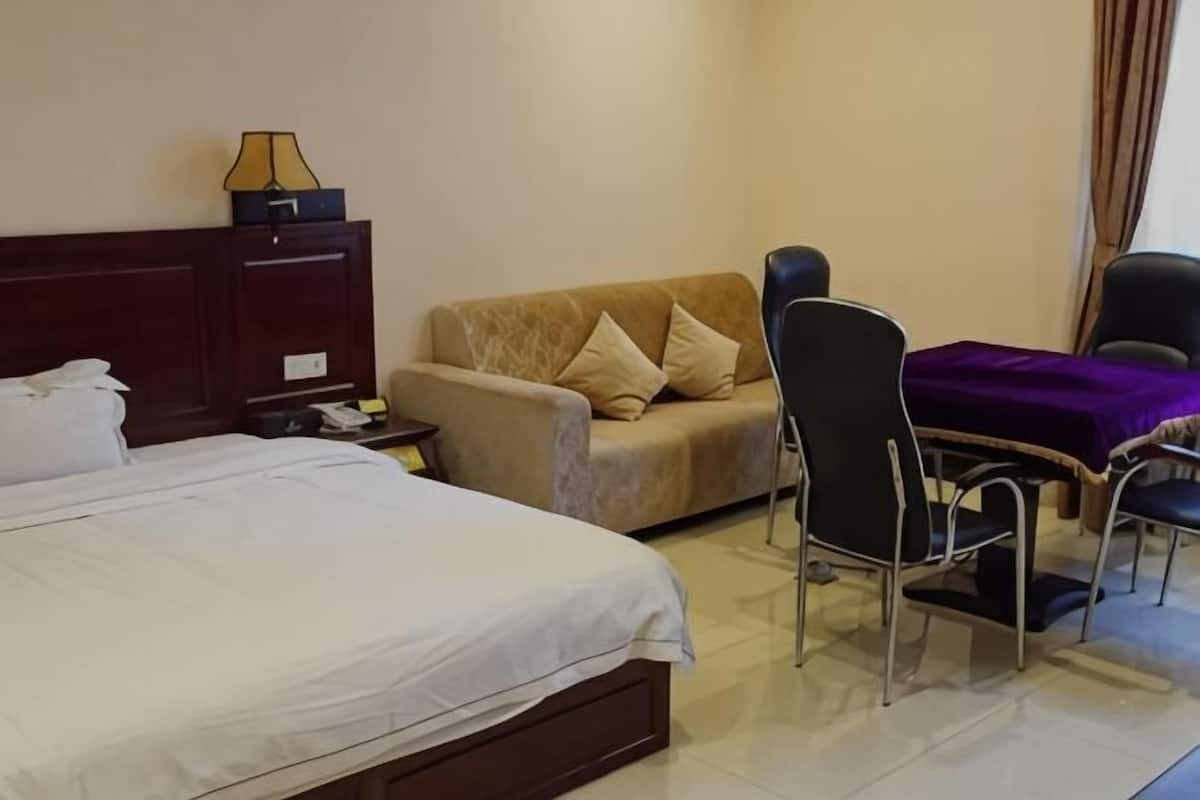 A hotel room with a bed, a sofa, a dining table with chairs, a lamp, and a nightstand.
