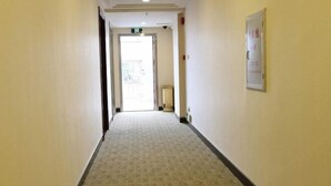 A hallway with patterned carpet, a door at the end, and a sign on the wall. - Hong Xin Business Hotel (Guangzhou)