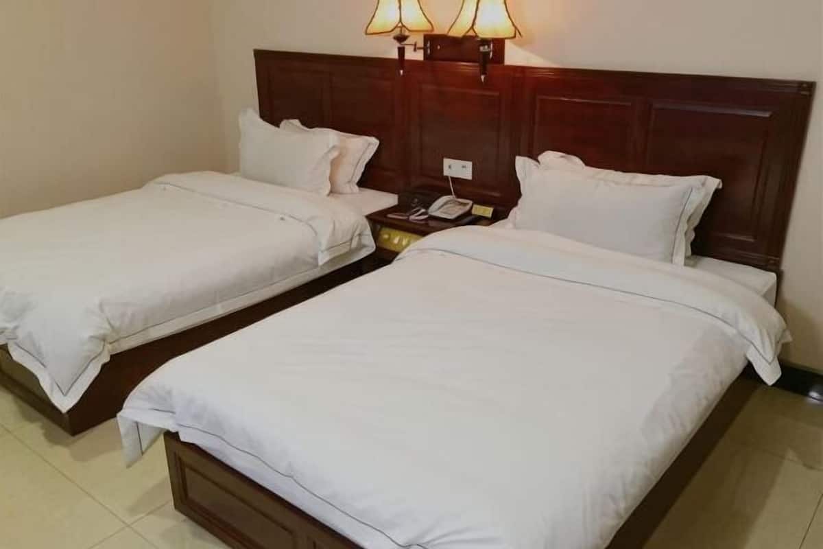 A hotel room with two single beds, a wooden headboard, bedside lamps, and a telephone on the nightstand.