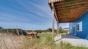 A wooden picnic table under a covered area with a blue house in the background. - Ocean Shores Retreat w/ Fire Pit - Walk to Beach! (Ocean Shores)
