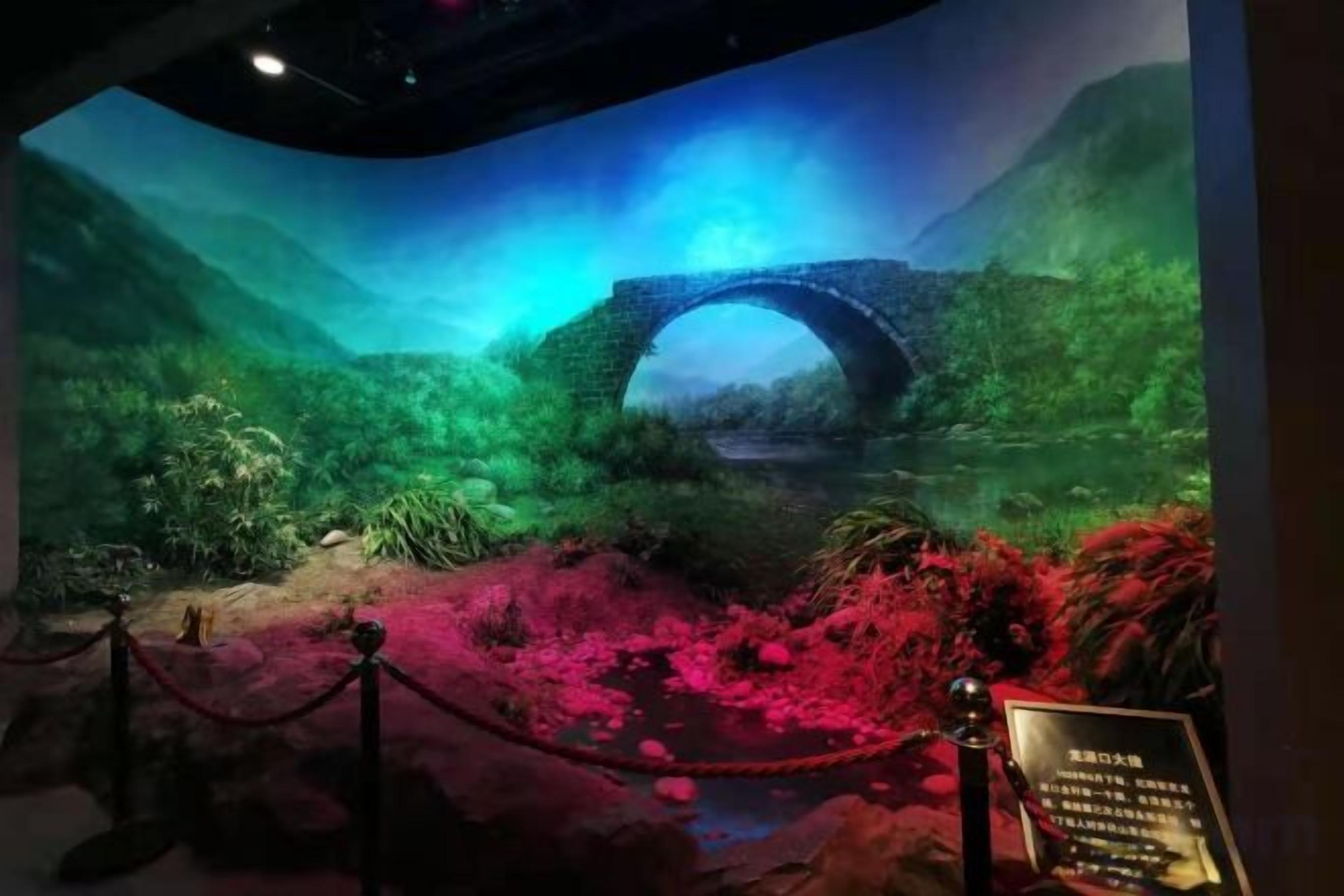Una exhibición de museo con un puente de piedra, abundante follaje y una zona alfombrada de color rojo.
