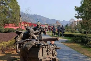 A statue of soldiers with a cannon, set in a landscaped area with a clear sky and mountains in the background. - Starlight Hotel(Jinggangshan Railway Station Store) (Jinggangshan City)