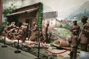 Una exposición de museo con un grupo de estatuas de bronce, una barrera de cuerda roja y un fondo de paisaje pintado.