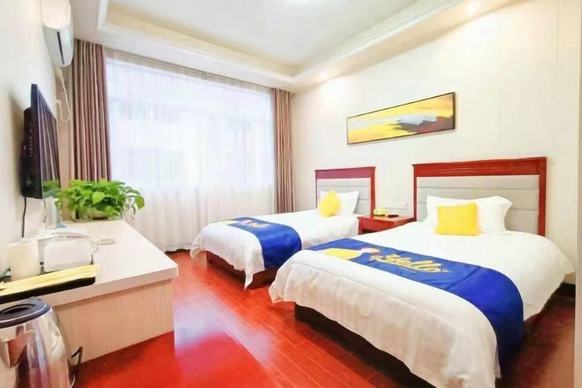 A hotel room with two beds, a desk, a TV, and a window with curtains.