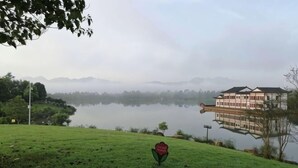 A serene lake with a building reflecting on the water, surrounded by greenery. - Starlight Hotel(Jinggangshan Railway Station Store) (Jinggangshan City)