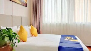 A hotel room with a bed, a plant, a painting on the wall, and a window with curtains. - Starlight Hotel(Jinggangshan Railway Station Store) (Jinggangshan City)