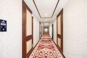 A long, narrow hotel corridor with a patterned carpet and wooden paneling on the walls. - Starlight Hotel(Jinggangshan Railway Station Store) (Jinggangshan City)