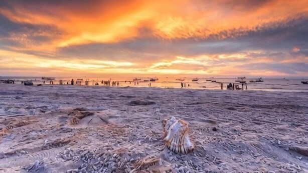 Una spiaggia al tramonto, con barche e un molo.
