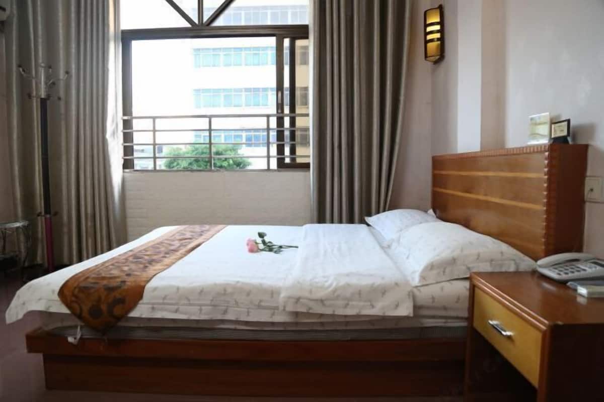 Ein Hotelzimmer mit einem Bett, einem Nachttisch mit Telefon, einem Fenster mit Vorhängen und Blick auf Gebäude.
