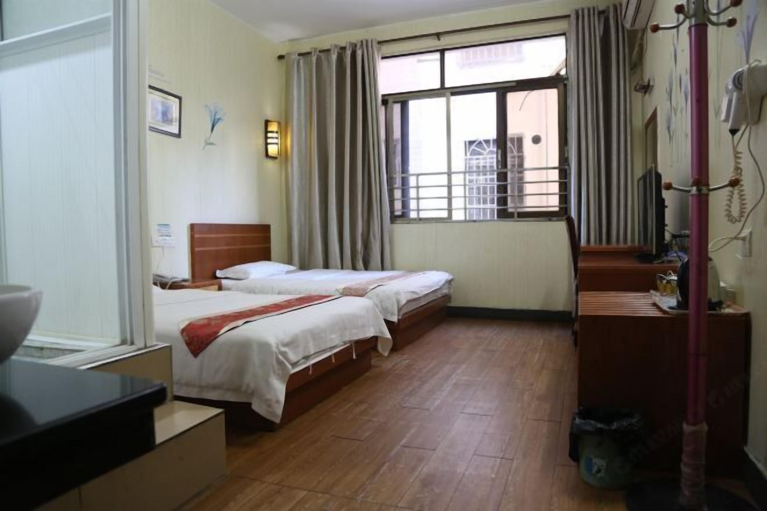 A hotel room with two beds, a desk, a window with curtains, and a view of the outside.
