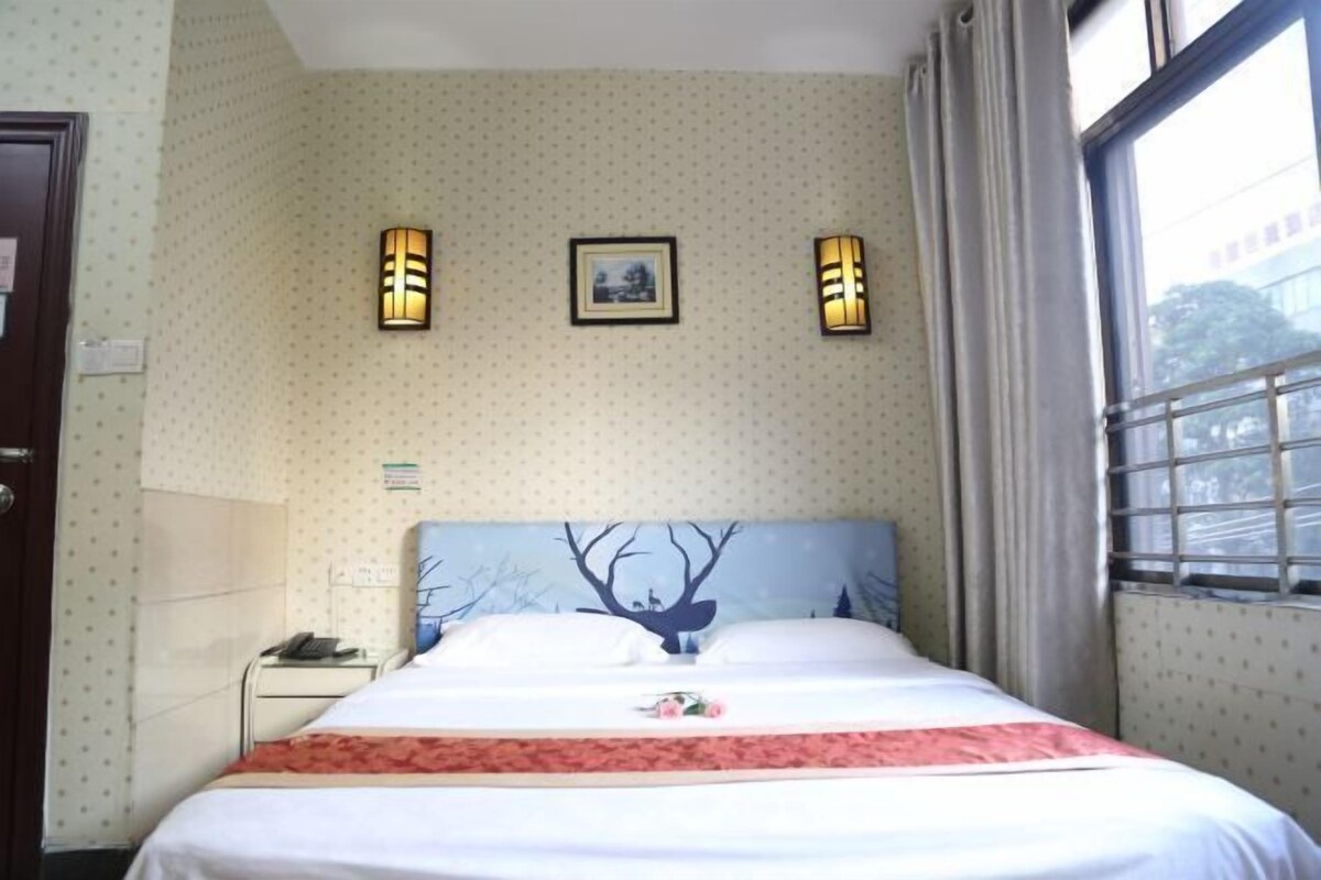 A hotel room with a bed, two wall-mounted lights, a framed picture, and a window with curtains.