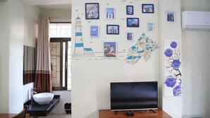 Una stanza con televisione, un lavandino bianco, una finestra con tende e decorazioni murali tra cui un faro e una mappa.
