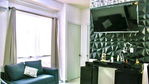 A modern living room with a sofa and a television mounted on a geometric-patterned wall. - Confort Condo with semi-Olympic pool, Wifi, AC, Grill, Balcony, Garden   (Playa del Carmen)