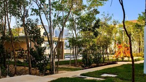 A landscaped area with trees, a playground, and a building with a flat roof. - Confort Condo with semi-Olympic pool, Wifi, AC, Grill, Balcony, Garden   (Playa del Carmen)
