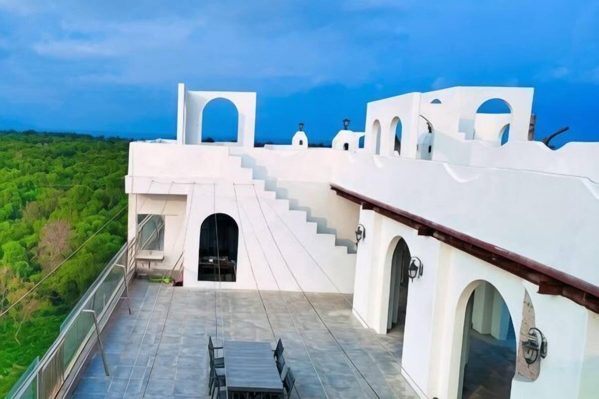 A white building with a staircase leading to a balcony, a table, and a chair on the balcony.