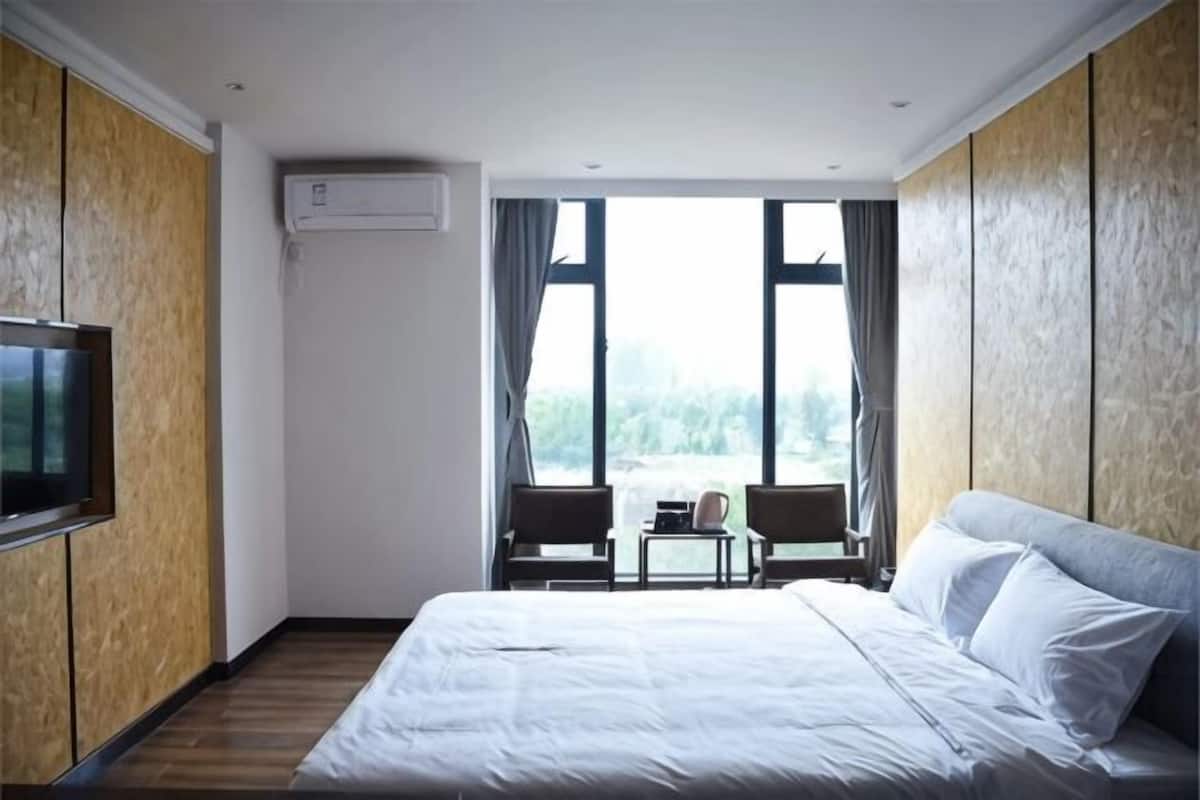A hotel room with a bed, a TV, a small table, and a view of the outdoors.