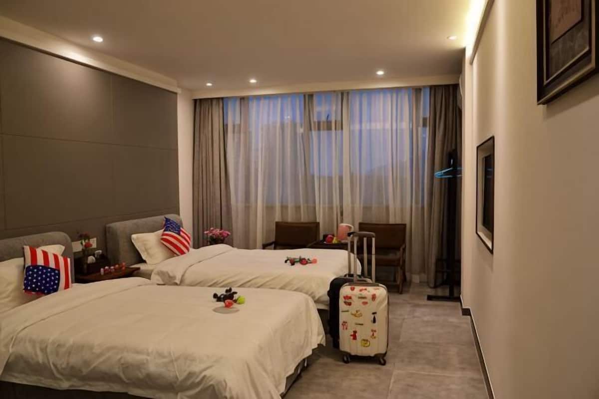A hotel room with two beds, a desk, a chair, and a suitcase.