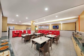 A restaurant with multiple tables and red booths, a buffet area, and a television screen.