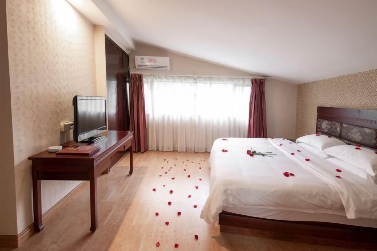 A hotel room with a bed, a TV, a desk, and a window with curtains.