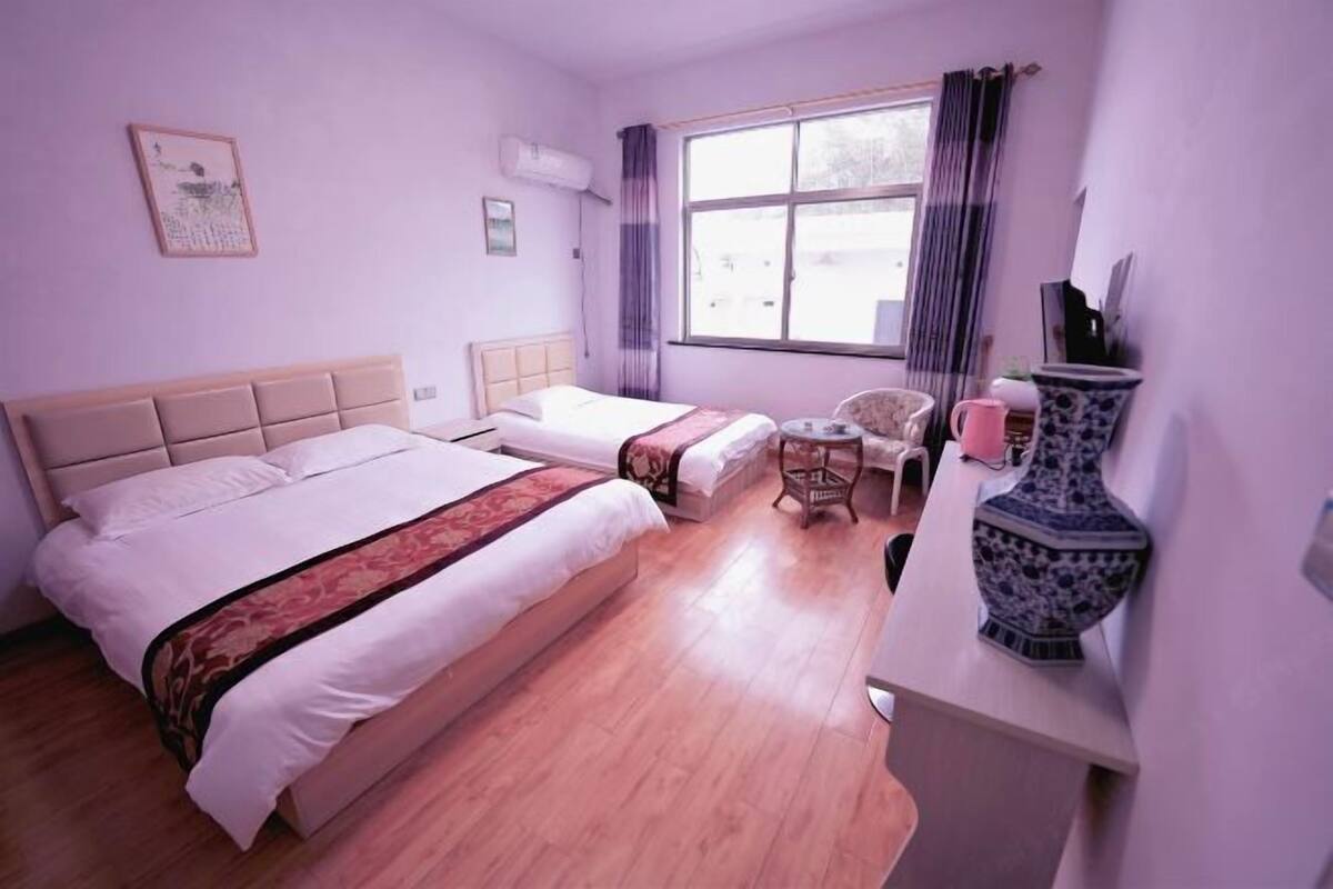 Une chambre d’hôtel avec deux lits, une petite table, une chaise, un vase décoratif et une fenêtre avec des rideaux.